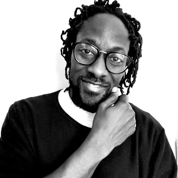A man with glasses and dreadlocks is posing for the camera.